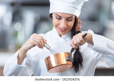 Pro woman works as a chef in the kitchen, whisking and holding a copper pan.