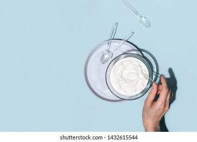 Probiotic Or Conventional Plain Low Fat Yogurt In Glass Bowl, Top Down View On Woman's Hand Putting Plastic Spoon In A Bowl Full Of Sour Cream Or Yogurt, Blank Space For A Text