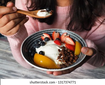 Probiotic And Fermented Food Theme Bowl Of Greek Yogurt Topped With Granola And Fresh Fruits Strawberries, Blueberries, Peach In Female Hand With Wooden Spoon. Healthy Eating Lifestyle Concept.