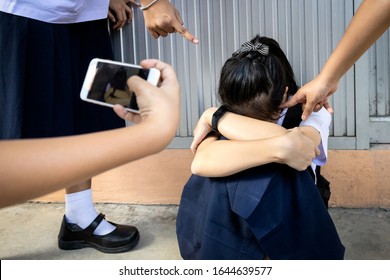 Problem Of Bullying At School,sad Stressed Asian Girl Student In Thai School Uniform Sitting On The Floor With Hands On Knees,scared,anxious Victim Of Bullying And Video Recorded On A Mobile Phone 