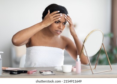 Problem Skin, Acne, Blackheads Concept. Angry Young African American Looking At Mirror, Touching Her Forehead, Removing Pimple, Black Lady Wrapped In Towel Applying Make Up, Home Interior