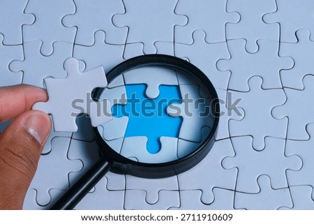 Problem solving concept with a hand holding the missing puzzle piece and a magnifying glass focusing on the missing gap of the puzzle for solution, idea and strategy