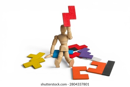Problem solving and creativity concept with a wooden mannequin sitting among colorful puzzle pieces and holding a red block up.
