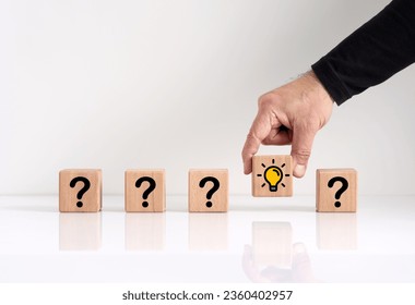 Problem solving and idea formation process. Male hand chooses the wooden cube with light bulb icon among the cubes with question mark icon.