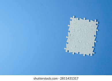 Problem solving and teamwork concept. Top view flat lay of a fully assembled blank white jigsaw puzzle placed on the right side of a light blue background with large copy space.