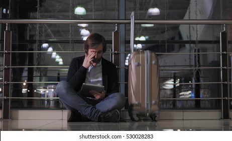 problem with transportation, delay of flight, depressed man  his luggage and tablet, headache  red eyes