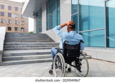 Problems with accessible environment for disabled people. Irritated impaired black man in wheelchair having no possibility to enter building without ramp, outdoors. Empty space