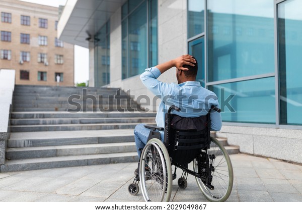 Problems with\
accessible environment for disabled people. Irritated impaired\
black man in wheelchair having no possibility to enter building\
without ramp, outdoors. Empty\
space