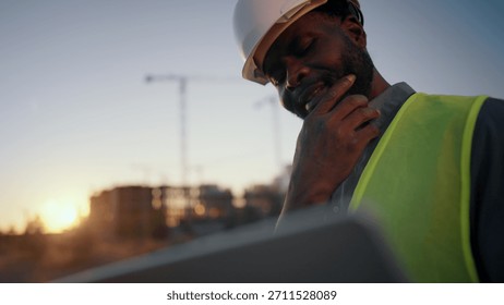 Problems at construction site, foreman looking at laptop display and thinking. Medium portrait of thoughtful builder or architect with computer, examining plant and drawing, engineer making decision