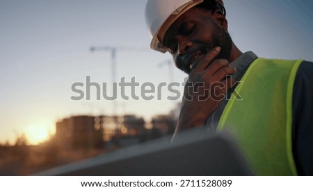 Problems at construction site, foreman looking at laptop display and thinking. Medium portrait of thoughtful builder or architect with computer, examining plant and drawing, engineer making decision