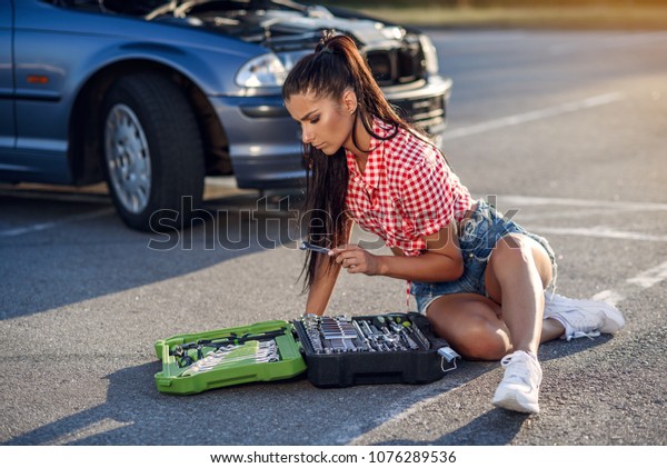 Problems with engine, confused driver.
Stressed woman sits near her broken down car. Woman with the box
with tools and wrenches waiting for an
assistant.