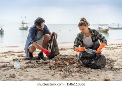 Problems of environmental pollution and oceans, a young couple in orange gloves cleans plastic and garbage in a black trash bag on a tropical beach in Thailand. - Powered by Shutterstock