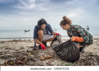 Problems of environmental pollution and oceans, a young couple in orange gloves cleans plastic and garbage in a black trash bag on a tropical beach in Thailand. - Powered by Shutterstock