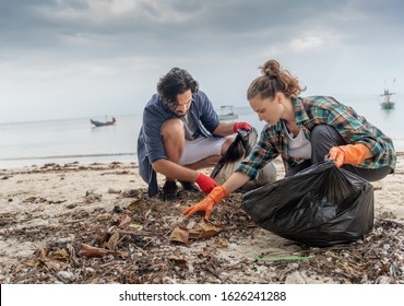 Problems of environmental pollution and oceans, a young couple in orange gloves cleans plastic and garbage in a black trash bag on a tropical beach in Thailand. - Powered by Shutterstock