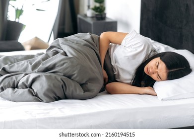 Problems With The Esophagus, Stomach Ache, Menstruation. Unhealthy Chinese Brunette Girl, Lying In A Bed, Holding Her Belly, Suffers From Pain In The Abdomen Or Stomach, Got Poisoned, Need Treatment