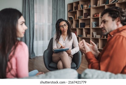 Problems In Family And Consultation With Psychologist. Sad European Millennial Couple Talking With Professional In Clinic Office Interior. Medical Support, Meeting With Doctor, Stress And Treatment