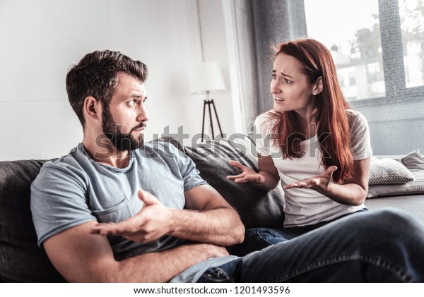 Problems in\
family. Unhappy cheerless young couple sitting together and talking\
to each other while having\
quarrel