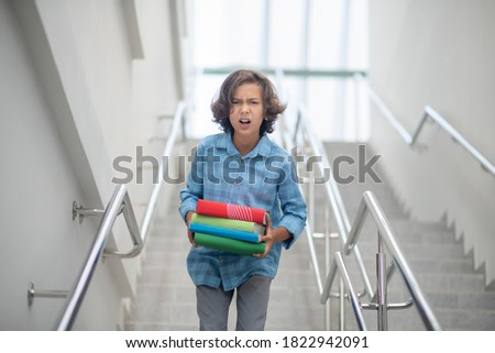 Problems at school. Upset schoolboy walking downstairs, carrying books