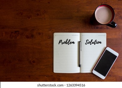 Problems and Solutions concept. A hot chocolate cup for drinking, smartphone, a pen and notebook on the wooden office desk written with text PROBLEMS and SOLUTIONS.