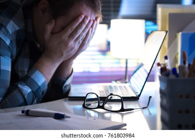 Problems at work. Sad, unhappy and tired man covering face with hands in office or home at night. Burnout, stress, workplace bullying or depression concept. Glasses on table.