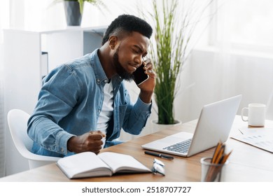 Problems at work. Stressed african american businessman talking on phone, looking at laptop screen and clenching fist in disappointment. - Powered by Shutterstock