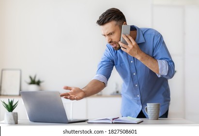 Problems At Work. Stressed Angry Businessman Emotionally Talking On Cellphone, Having Troubles With Laptop Program, Speaking With Customer Support, Displeased Man Looking At Computer Screen