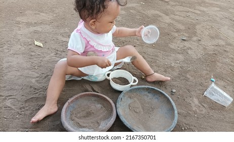 PROBOLINGGO, INDONESIA - June 14, 2022 : A Toddler Sitting On The Ground Playing With White Plastic Cups, Bowls And Spoons