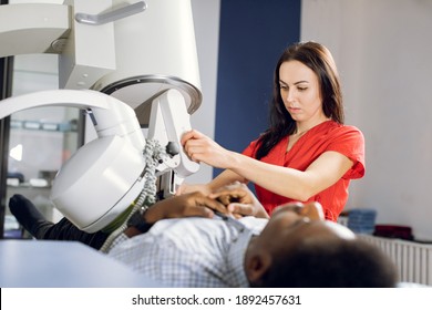Procedure of extracorporeal shock wave lithotripsy in modern urology medical center. Close up of pretty Caucasian woman doctor providing stone treatment for black male patient using lithotripter