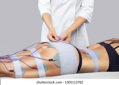 The procedure of myostimulation on the legs and buttocks of a woman in a beauty salon. Caring for the body, reducing excess weight.