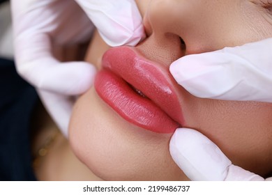 procedure of permanent make-up of the lips with the help of a typewriter, the master gently holds the lips of the model with his fingers