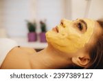 Procedure for skin care. Doctor in cosmetology office applies an yellow gold alginate mask to the face of young pretty woman. High quality photo