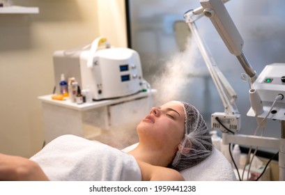 The Procedure Of Steaming The Skin Of The Face Of Young Woman Before Cleaning The Skin In A Beauty Salon.