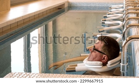 The procedure of underwater traction of the spine in the pool. A man hangs in the water, with support behind his neck. Due to its own weight and goose on the legs, a soft stretching of the spine.