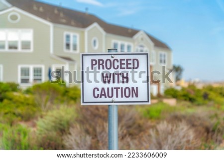Proceed with caution sign post in a residential area at Southern California. Warning sign on a metal pole against the blurry bushes and mint green townhouse building background.