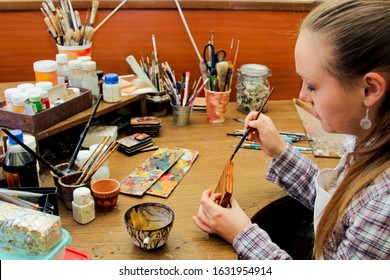 Process Of Aging Of A Wooden Picture, Processing Of Wood, Toning With Wood Stain. Girl Artist Paints A Picture In The Studio. Brushes And Paints On The Background.