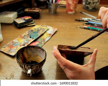 Process Of Aging Of A Wooden Picture, Processing Of Wood, Toning With Wood Stain. Girl Artist Paints A Picture In The Studio. Brushes And Paints On The Background.