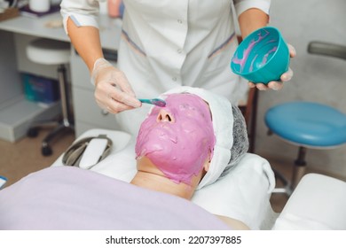 The process of applying an alginate face mask. cosmetologist holding a spatula. A woman lying on a couch in the cosmetologist's office. Facial skin care in a beauty salon