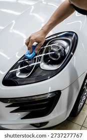 The process of applying a nano-ceramic coating for hydrophobic effect on the white car's door by a male worker with a sponge and bottle of chemical composition. Auto service industry. Nano ceramic. 