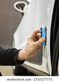 The process of applying a nano-ceramic coating for hydrophobic effect on the white car's door by a male worker with a sponge and bottle of chemical composition. Auto service industry. Nano ceramic. 