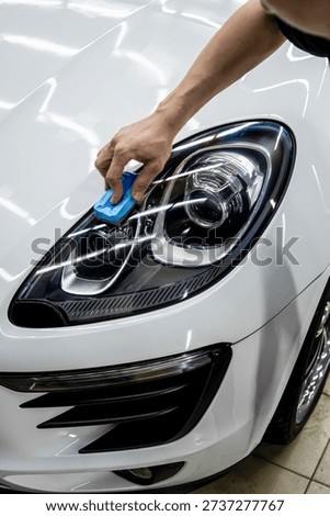 The process of applying a nano-ceramic coating for hydrophobic effect on the white car's door by a male worker with a sponge and bottle of chemical composition. Auto service industry. Nano ceramic. 