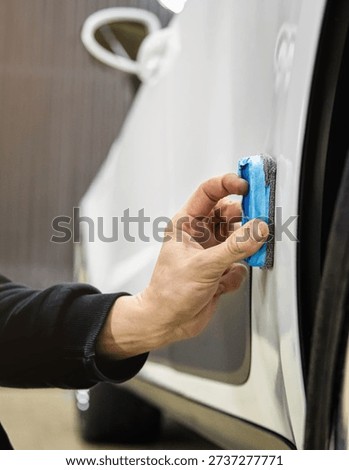The process of applying a nano-ceramic coating for hydrophobic effect on the white car's door by a male worker with a sponge and bottle of chemical composition. Auto service industry. Nano ceramic. 