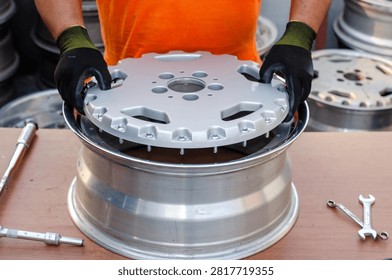 The process of assembling the center part of a car rim made of aluminum alloy 3-piece split wheel, by the hands of a technician using a protective shield on a workshop workbench. 