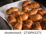 The process of baking bread: Baker using a spatula and glove to arrange freshly baked golden salt bread (Shio Pan) on a tray
