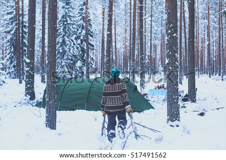 A process of camping in winter forest, setting a tent covered in snow, making a bonfire campfire and cooking food with portable gas cooker and fire, snowy landscape