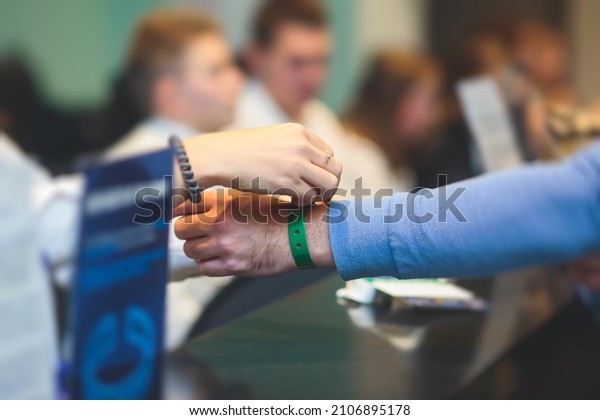 Process of checking in on a conference congress forum\
event, registration desk table, visitors and attendees receiving a\
name badge and entrance wristband bracelet and register electronic\
ticket, 