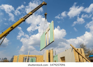 Process Of Construction New And Modern Modular House From Composite Sip Panels. Crane With Wall Part Against Blue Sky Background