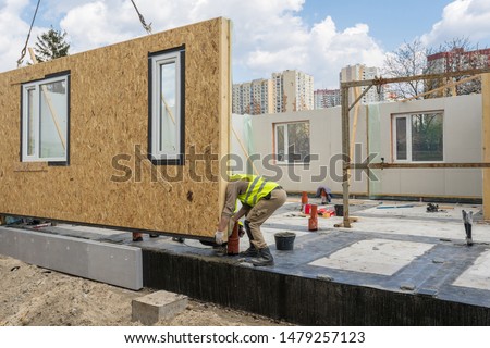 Process of construction new and modern modular house from composite sip panels. Worker man in special protective uniform wear working on building development industry of energy efficient property