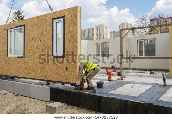 Process of construction new and modern modular\
house from composite sip panels. Worker man in special protective\
uniform wear working on building development industry of energy\
efficient property