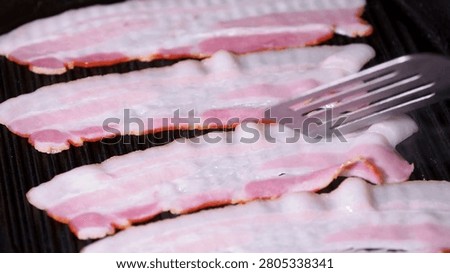 the process of cooking bacon slices on the grill. Chef grilling strips of bacon. Cook and prepares delicious bacon strips for eating in closeup.