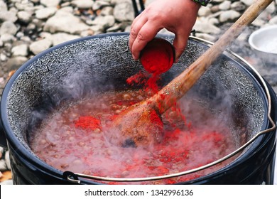 The Process Of Cooking Dishes Chile Con Carne. Adding Red Ground Pepper. You Can See The Hand Of The Cook And A Wooden Spoon